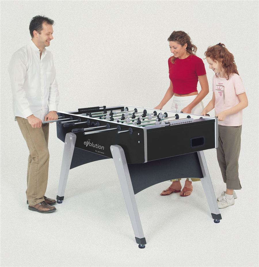 Drei Personen spielen gemeinsam an einem schwarzen Tischfußballtisch mit silbernen Beinen, lächelnd und konzentriert.