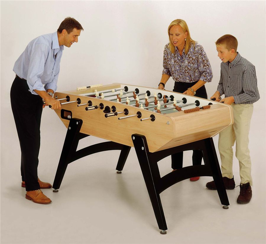 Drei Personen, zwei Erwachsene und ein Kind, spielen gemeinsam an einem modernen Tischkicker aus Holz mit schwarzen Beinen.