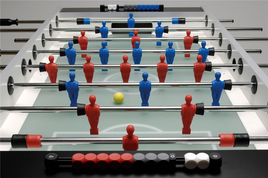 Tischkicker mit roten und blauen Spielfiguren, gelber Ball in der Mitte, Zählleisten oben und unten am Spielfeldrand.