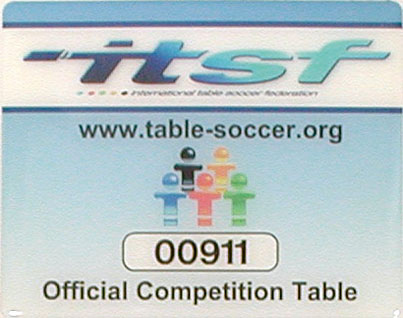 ITSF-Plakette mit Logo, bunter Figuren-Grafik, Seriennummer 00911 und Text „Official Competition Table“ auf blauem Hintergrund.