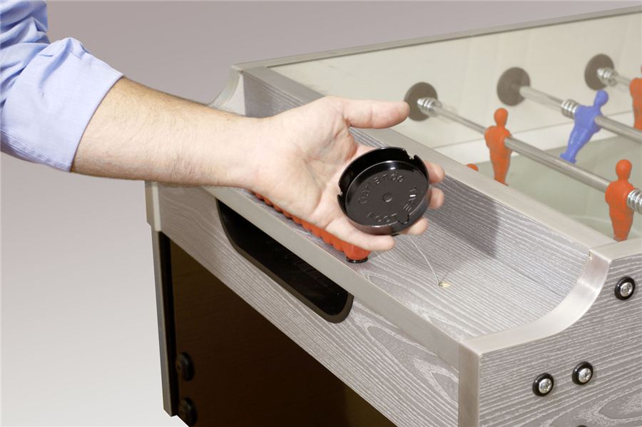 Eine Hand hält einen schwarzen Puck über einem Tischkicker mit roten und blauen Spielfiguren.
