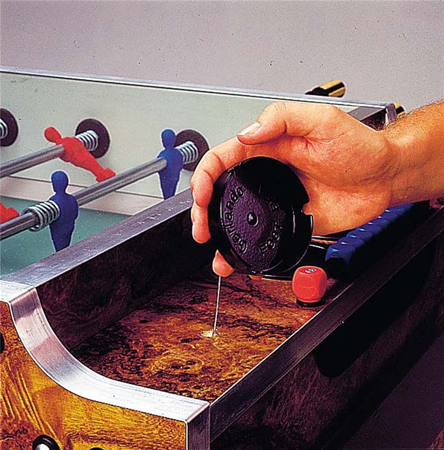 Hand dreht eine Schraube in einen Tischkicker, um die Spielfläche zu befestigen.