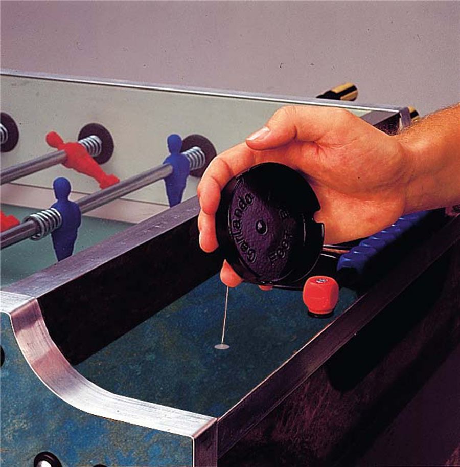 Eine Hand hält eine Dose Silikonöl über einem Kicker-Tisch, um die Stangen zu schmieren.