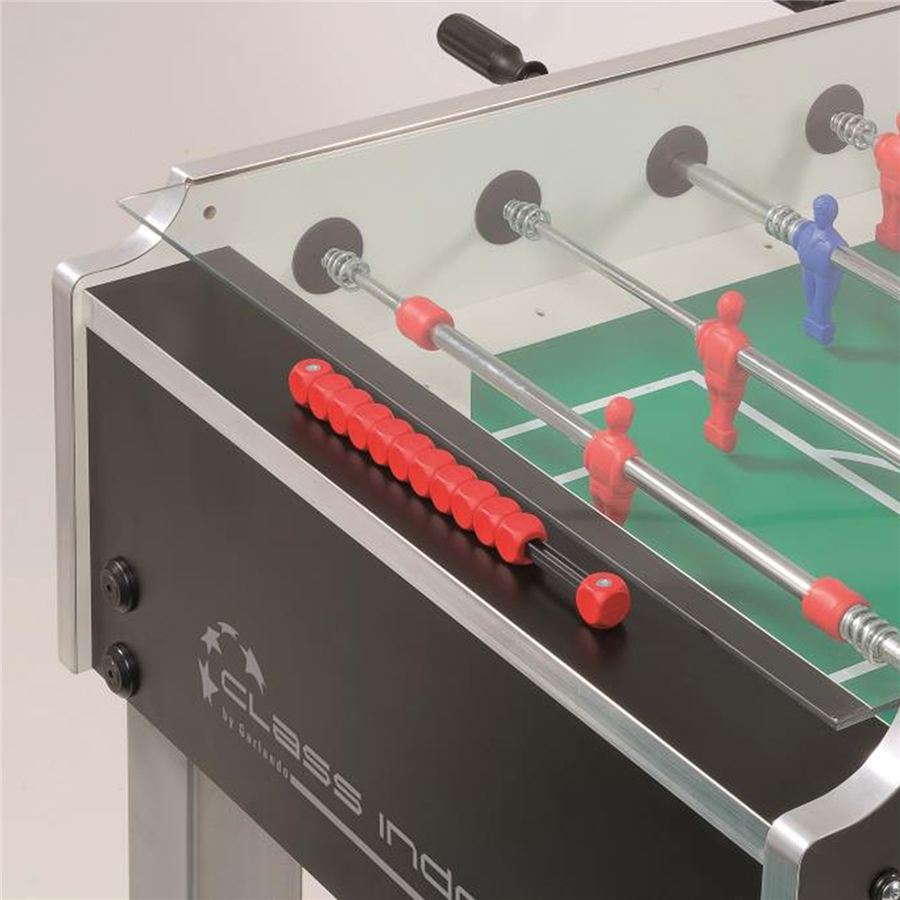 Detailansicht eines Kickertisches mit roten und blauen Spielfiguren, Glasabdeckung und rotem Griff an der Spielstange.