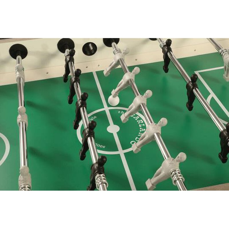 Tischfußballspiel mit schwarzen und weißen Spielfiguren auf grünem Spielfeld, Ball in der Mitte.