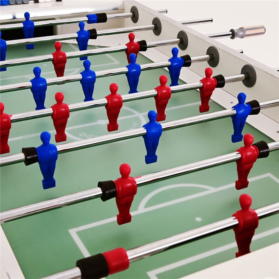 Tischkicker mit roten und blauen Spielfiguren auf grünem Spielfeld, Metallstangen und sichtbaren Torbereichen.